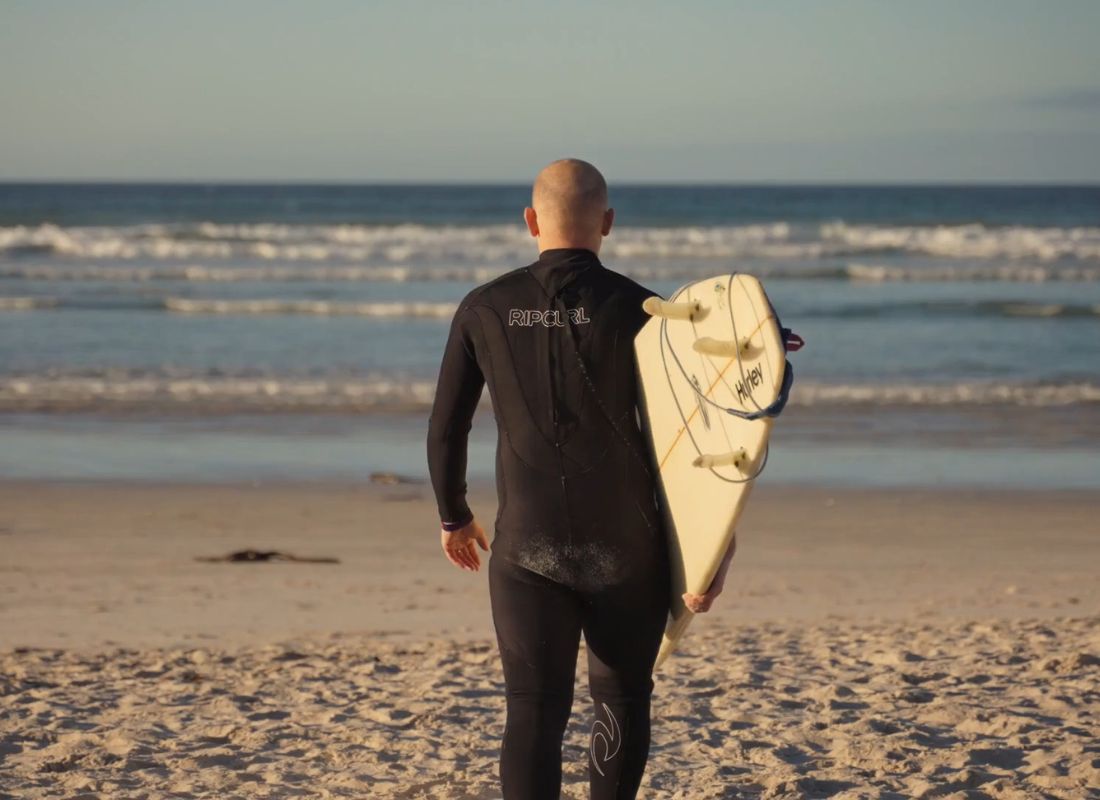 momak u odelu za surfovanje nosi dasku i ide ka moru