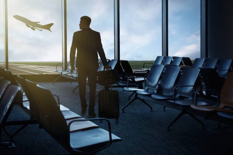 momak stoji na aerodromu sa prtljagom u rukama i gleda kako avion poleće